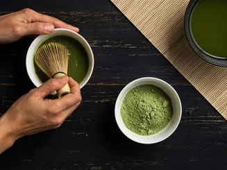 Manos preparando té matcha con un batidor de bambú