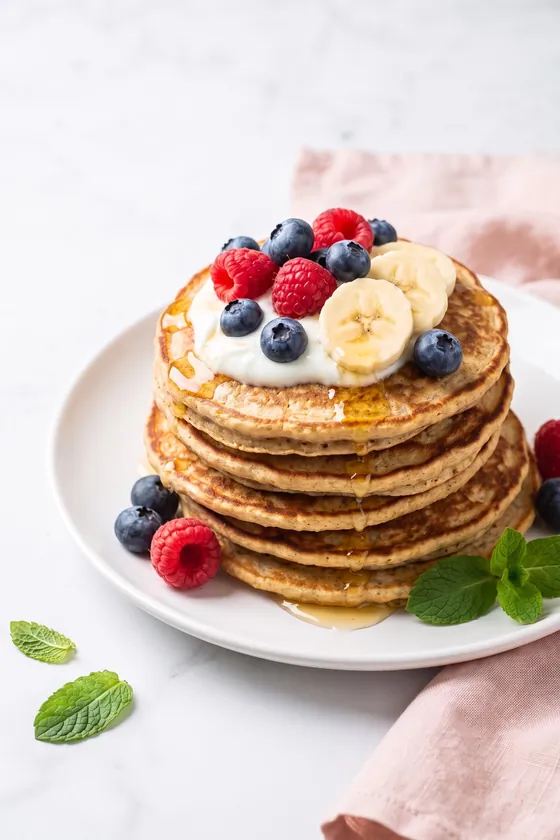 Tortitas de avena con yogur griego, arándanos, frambuesas, plátano y un hilo de miel