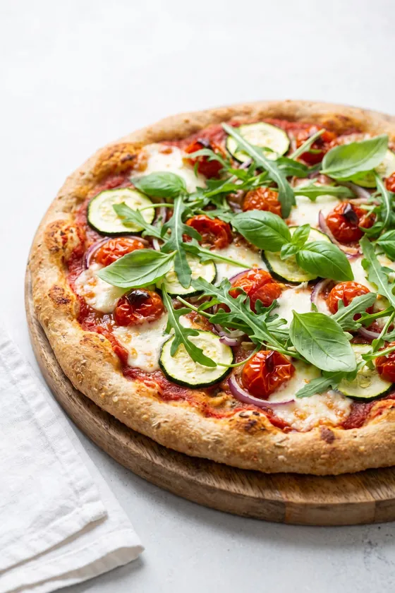 Pizza casera de masa integral con mozzarella, tomates cherry, calabacín, rúcula y albahaca