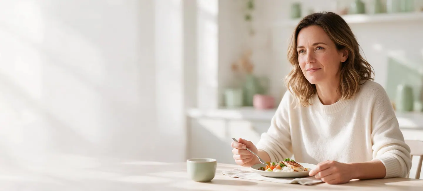 Mujer sentada con tranquilidad ante un plato de comida normal en una cocina luminosa